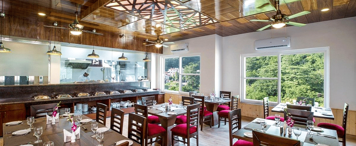 Full view shot of the restaurant at Regenta Inn DLS with neatly arranged dining tables with ample of natural lighting inside.