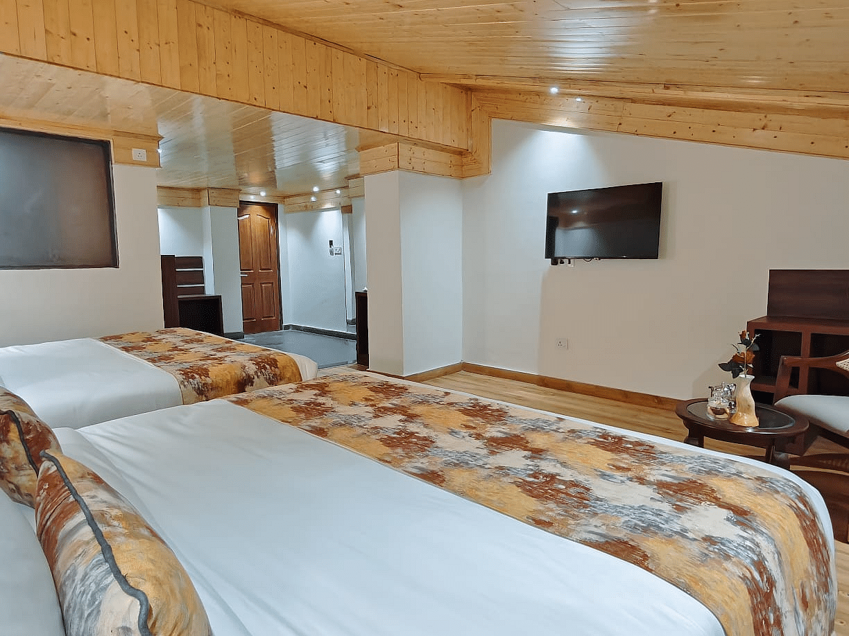 A modern, well-appointed room featuring two beds with crisp white linens and patterned runners, a wall-mounted tv, and an elegant wooden ceiling - Sumitel JB Park, Darjeeling