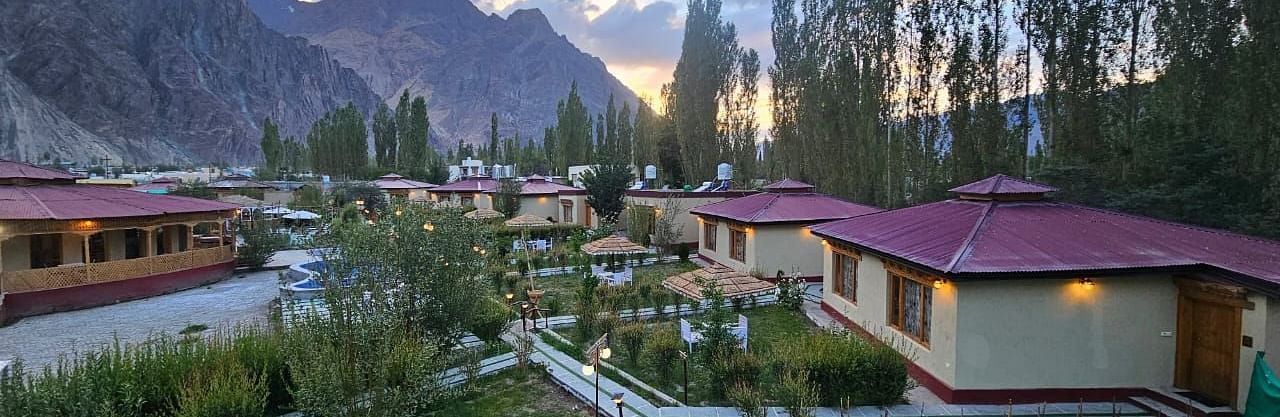 Panoramic view of White Sand Resort, Ladakh with cabins, trees, mountains, and a pathway.