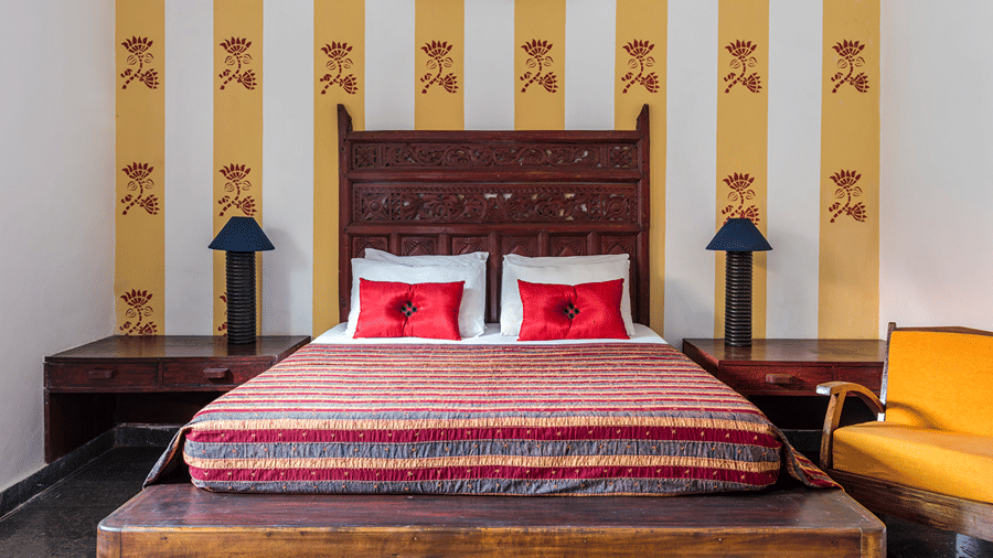 Double bed with red patterned bedding, a carved wooden headboard and matching bedside tables against striped walls.