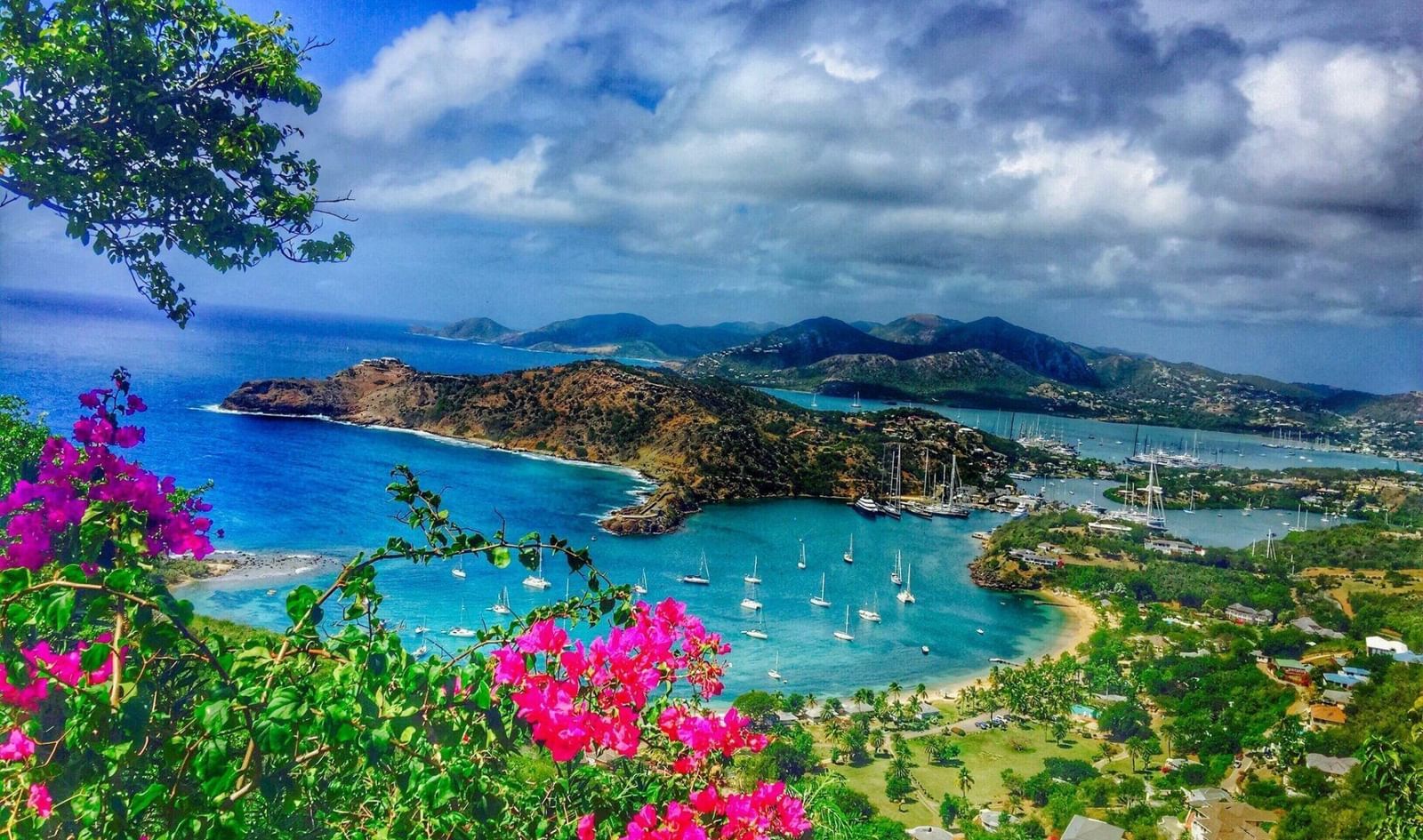 Stunning panoramic view of a bay with turquoise water, lush green hills, and vibrant pink flowers - Tamarind Hills Resort and Villas - Antigua