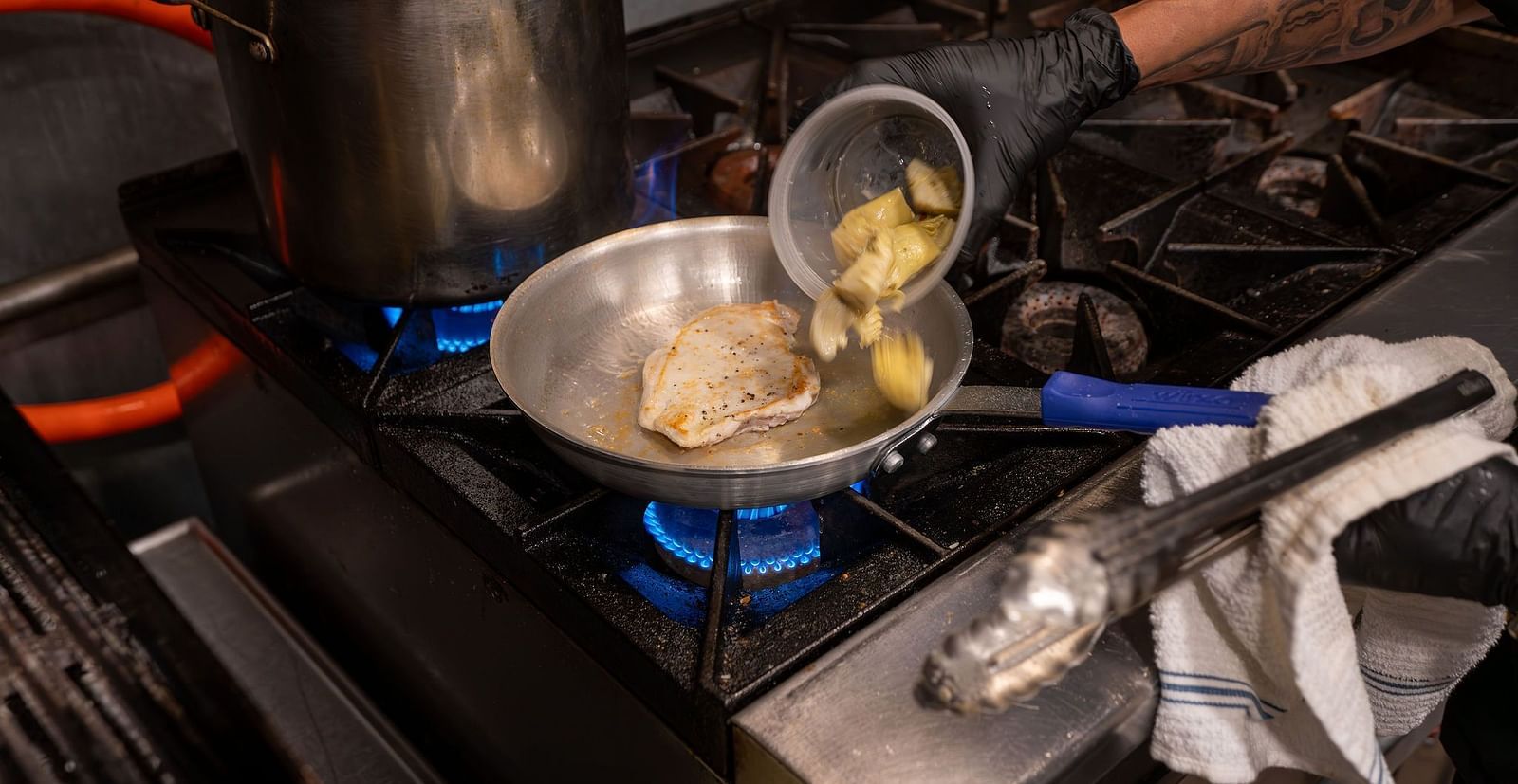 A close up shot of a chef heating up a dish on a burner - The Groveland Hotel.