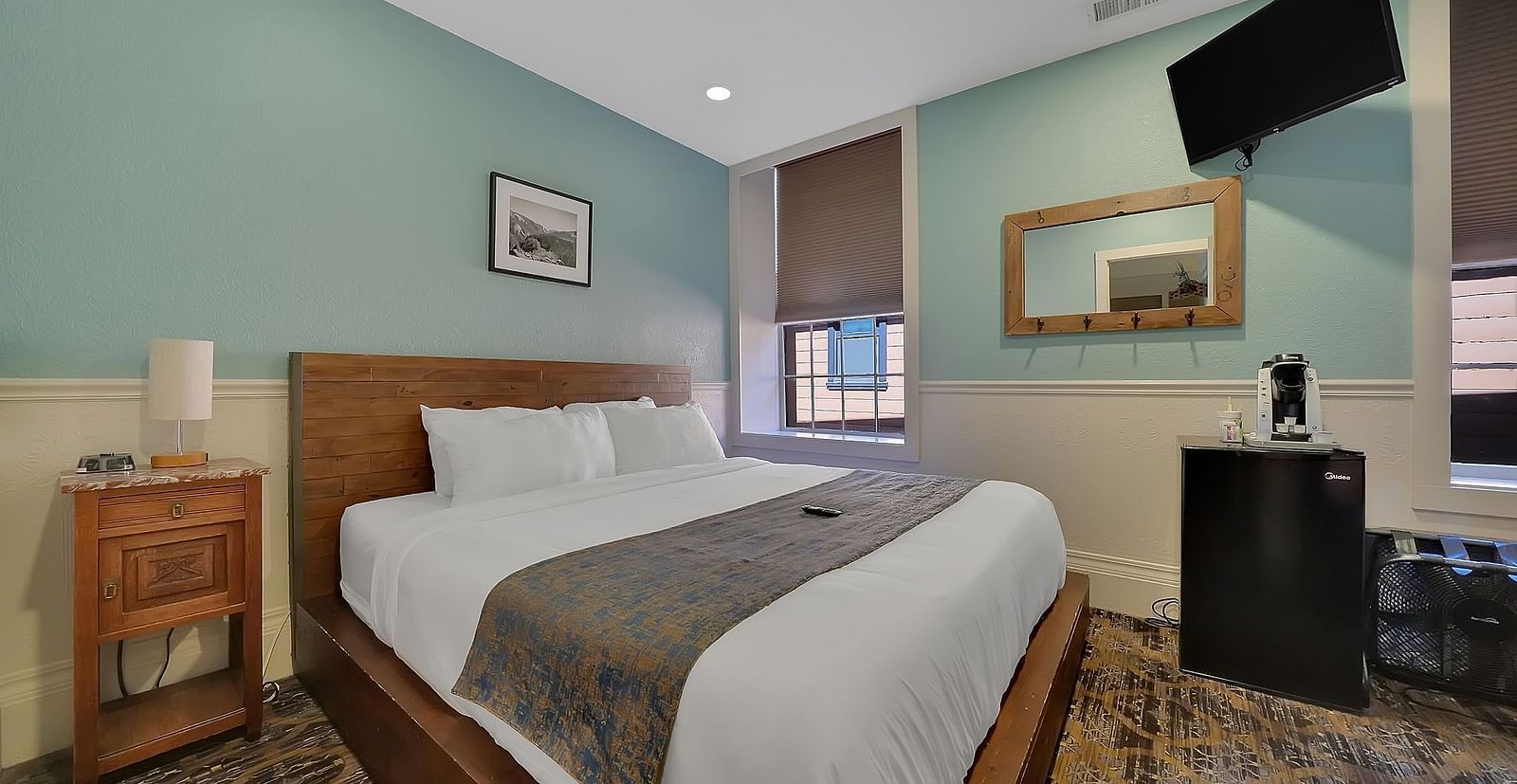 A comfortable room at The Groveland Hotel with sage green walls, wooden bed, blue patterned runner, TV, and convenient coffee station.