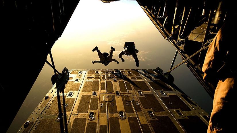 Two people jumping out of an airplane with the sun's rays in view.
