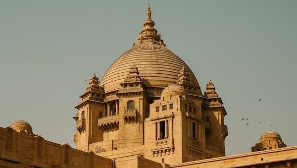 A facade image of a brown palace with sunlight hitting on a part of the structure