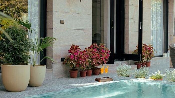 Open glass doors leading to a small pool area surrounded by flower pots and blooming pink flowers at Karma Chalets.