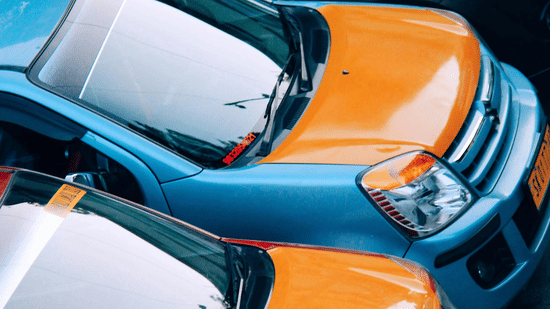 An overhead, tight-crop view of several brightly coloured cars, including orange and blue models, parked closely together.
