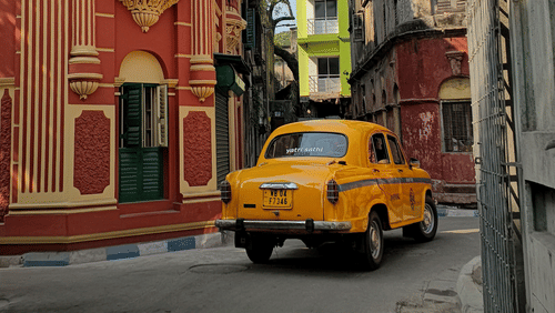 Classic yellow taxi driving through a heritage street in Kolkata.