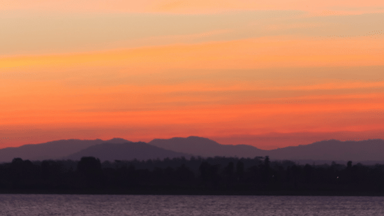 A twilight view of a boat travelling towards the camera with different hues in the sky after the sunset.