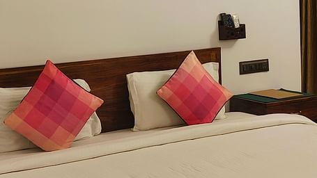 Front view of a double bed with two pink pillows kept on it and hexagonal frames hanging on the wall in 101 non-ac room at Ananda Holiday Home, Wayanad 1