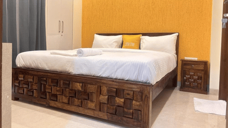Bedroom of Lime Tree Hotels & Service Apartment Private Limited featuring a carved wooden bed frame and a mustard headboard.