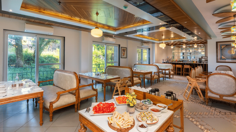 A spacious dining area at Quality Inn with multiple tables and chairs, a buffet table with food, and large windows offering a view of greenery.