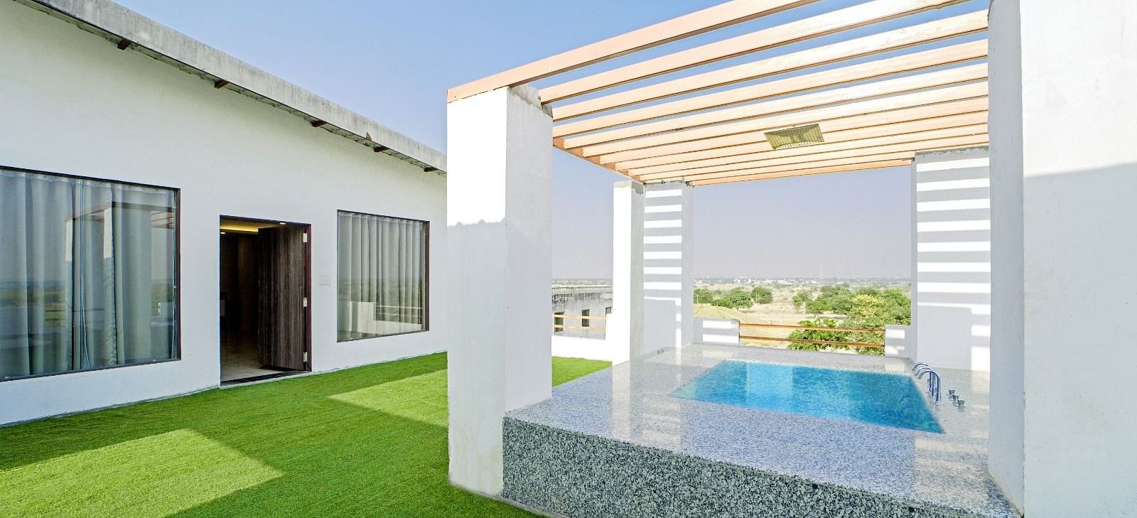 Poolside lounge area at Grassfield Riveria Resort, Jaipur, featuring a shaded seating space and views of the swimming pool.