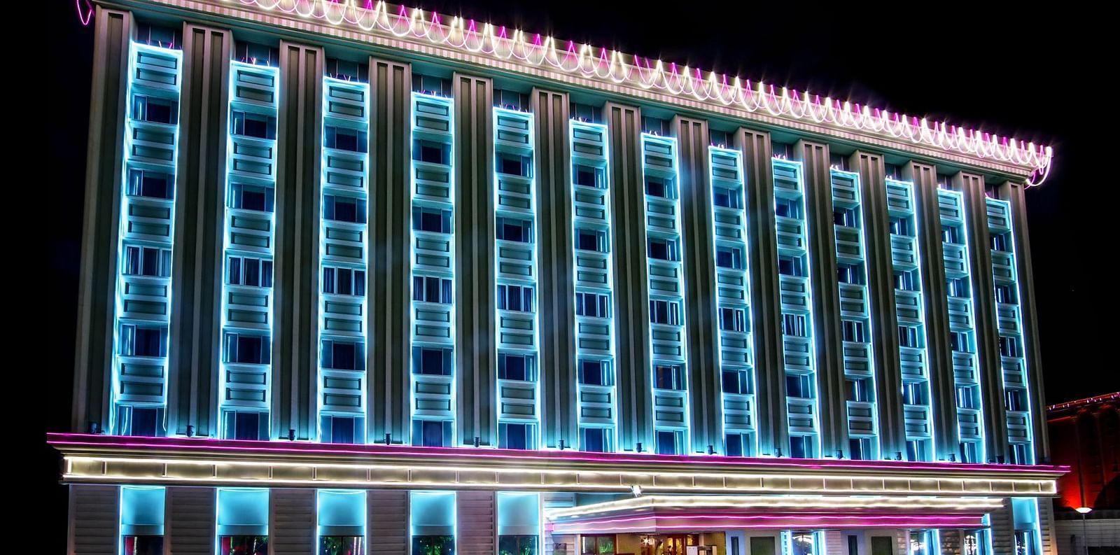 The facade of a hotel illuminated with blue neon lights at night - Tara, Comfort Hotel in Hyderabad - Ramoji Film City.