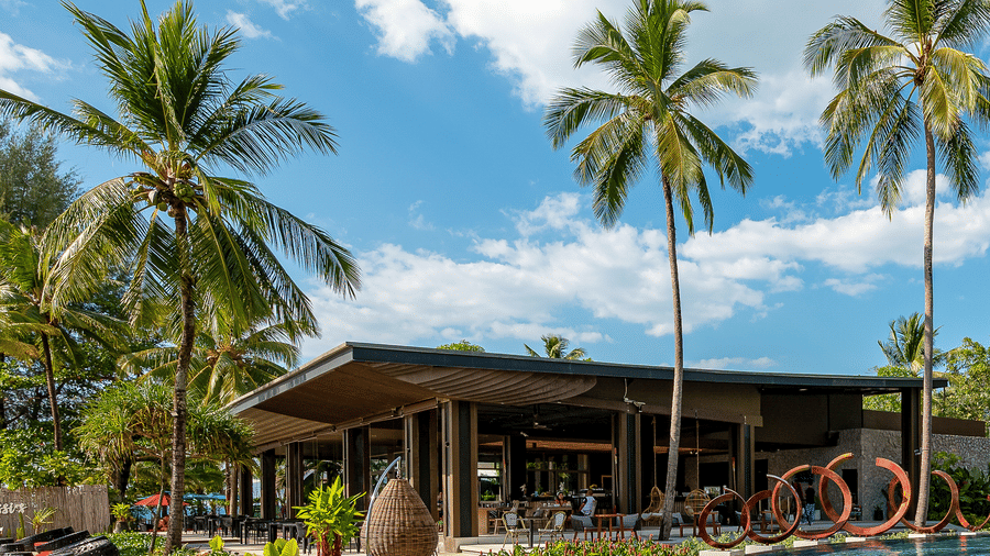 A modern resort building surrounded by tall palm trees and landscaped gardens under a clear sky at Ramada Resort by Wyndham Khao Lak.