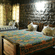 A rustic bedroom with stone walls featuring wooden beds adorned with colourful patterned quilts and warm lighting.