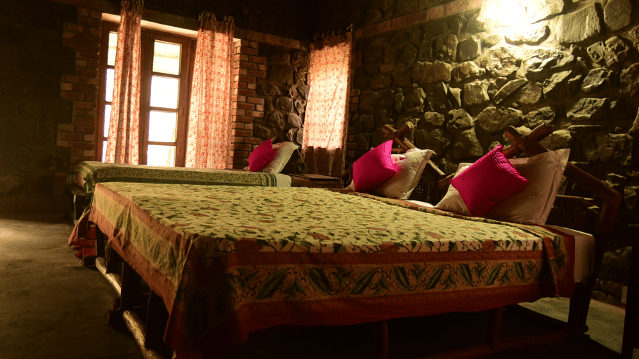 A cosy bedroom with rustic stone walls, beds made with patterned linens, bright pink pillows, and warm ambient lighting.