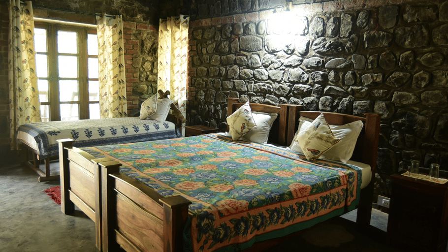 A rustic bedroom with stone walls featuring wooden beds adorned with colourful patterned quilts and warm lighting.