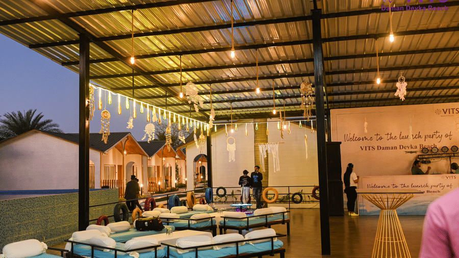 A view of the seating arrangement at Urban Dhaba, with a reception desk, dream catchers, LED lights and people in view at VITS Daman Devka Beach. Book direct through the website for the best hotel deals in Daman.
