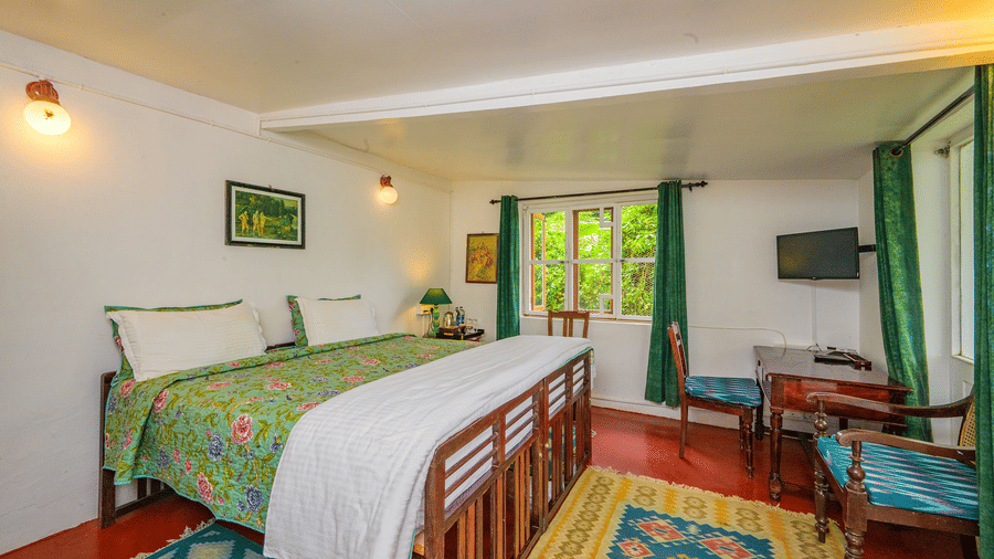 Wide view of the Camphor room at Wallwood Garden - 19th Century, Coonoor showing a double bed, writing desk, chairs and window seating.