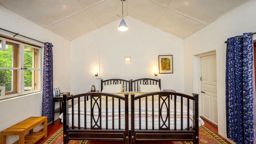 Front view of the Cherry Blossom room at Wallwood Garden - 19th Century, Coonoor showing twin beds, bedside lighting and large windows.