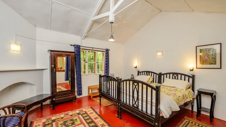 Spacious Cherry Blossom room at Wallwood Garden - 19th Century, Coonoor with wardrobe, seating chair, rugs and twin bed layout.