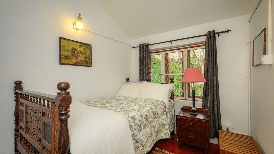 Red Cedar room at Wallwood Garden - 19th Century, Coonoor with a carved wooden bed, bedside table, soft lighting and garden-facing window.
