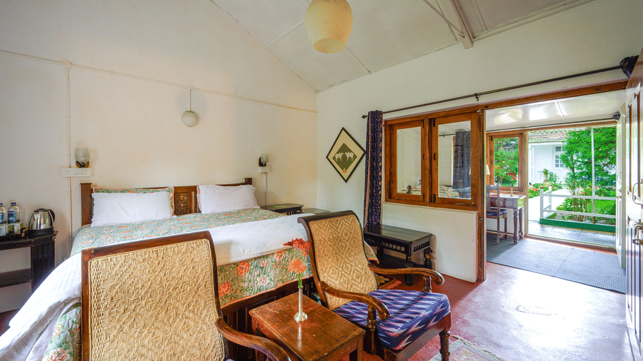 Silver Oak room at Wallwood Garden - 19th Century, Coonoor featuring a double bed, cane chairs, wooden furniture and garden-facing doorway.