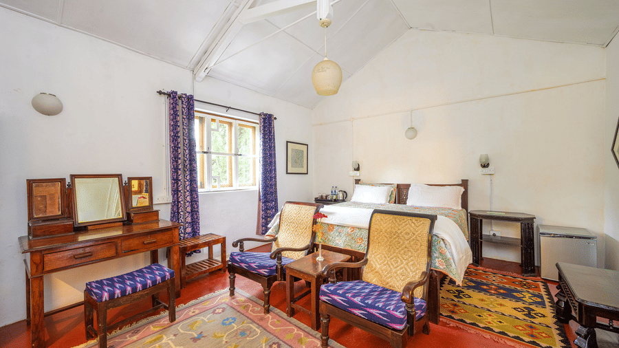 Spacious Silver Oak room at Wallwood Garden - 19th Century, Coonoor with wooden dressing table, seating chairs and patterned rugs.