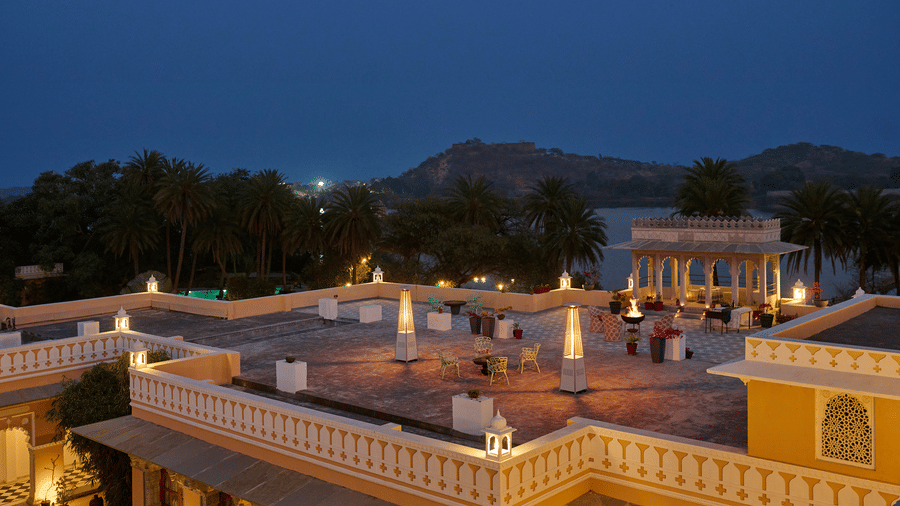 Elevated evening view of the rooftop courtyard at Dev Shree, Deogarh, featuring illuminated seating areas, a heritage pavilion, palm trees, and serene views of the surrounding landscape.