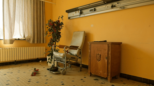 A room with yellow walls, a chair, a wooden cabinet, a potted plant, and a window with curtains at best resort in Bangalore.