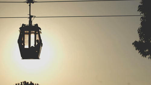 A cable car carrying two people silhouetted against a setting sun.