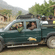 A green safari pickup truck carrying passengers near cottages in a mountainous resort setting.
