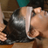 A woman lying down with a protective forehead band while receiving an Ayurvedic oil head massage from a therapist.