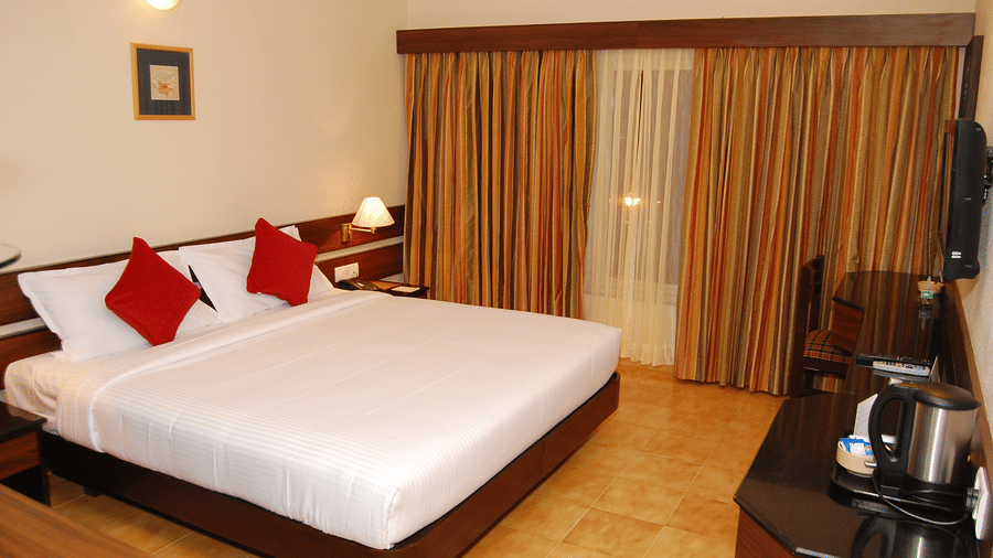 The spacious Deluxe bedroom at Green Pastures, Kodai, showcasing a magnificent large bed with crisp linens, accented by decorative pillows, and complete with a convenient hot beverage station near the window.