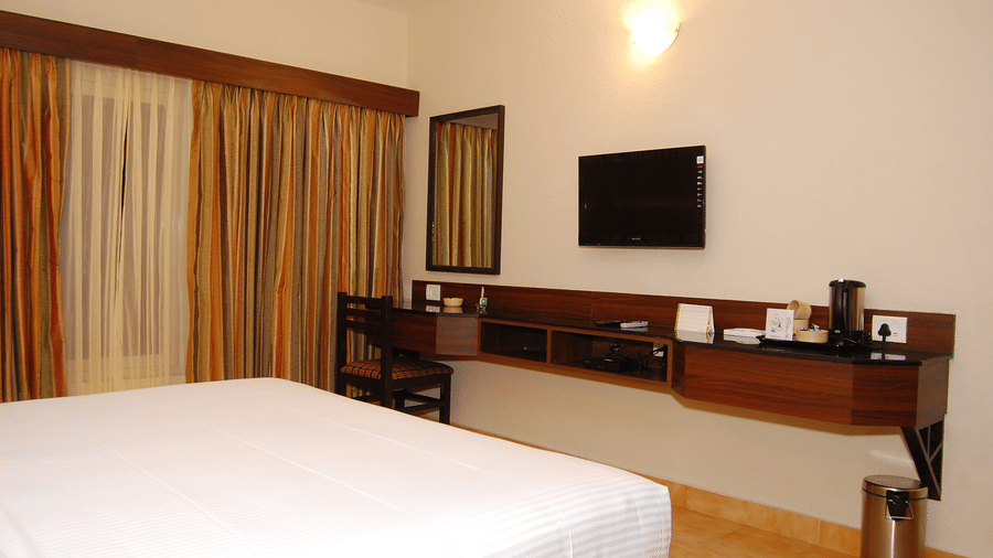 A welcoming accommodation at Green Pastures, Kodai, showcasing a double bed, sheer patterned window coverings, and a modern floating desk, and a wall-mounted television.