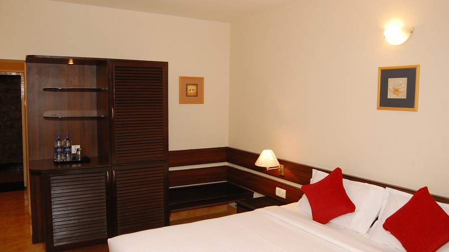 An Elegant bedroom interior Deluxe Room at Green Pastures, Kodai, featuring a beautifully prepared bed with decorative pillows, an integrated shelving unit, and warm wall sconce lighting above the headboard.
