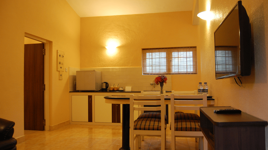 Separate area with wooden dining table and chairs, kitchenette setup with sink and counter, and hanging light in a suite at Green Pastures, Kodaikanal.