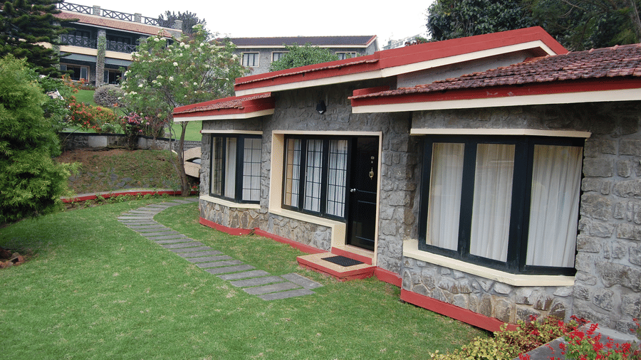 Exterior view of stone building with red roof and green lawn, garden surrounding ground level rooms at Green Pastures, Kodaikanal.
