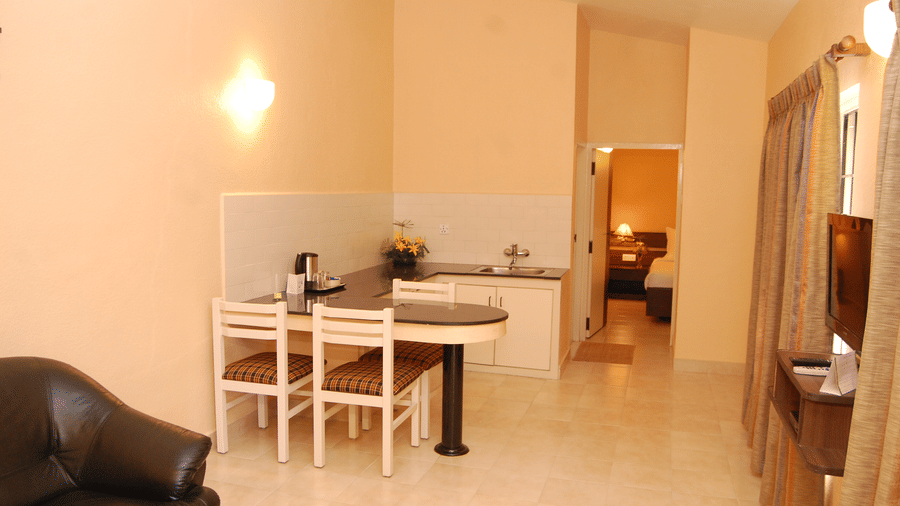 Spacious suite seperate living area with a white dining table and chairs, black sofa, beige walls, and a kitchen area at Green Pastures, Kodaikanal.