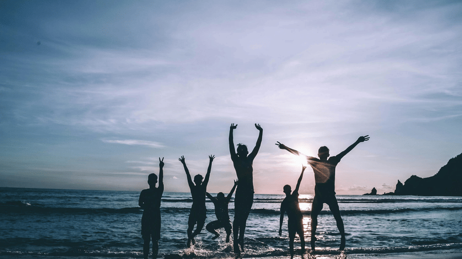 A group of friends jumps joyfully in the shallow water on a beach at dusk.