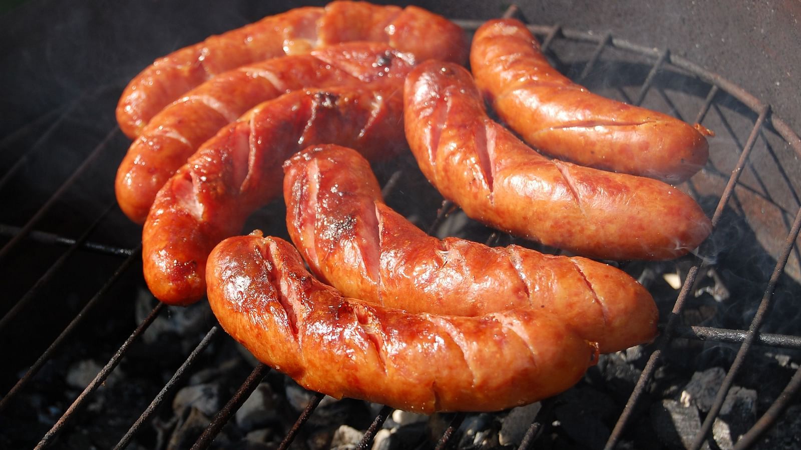An overview of cut sausages kept on a grill with the top part already cooked.