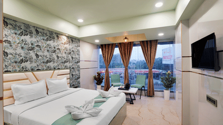 A king size bed in Deluxe Room with large windows overlooking the city at Hotel Regal Heaven, Pune.