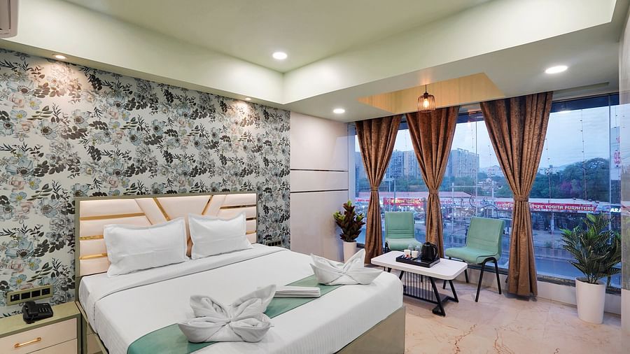 A king size bed in Deluxe Room with large windows overlooking the city at Hotel Regal Heaven, Pune.
