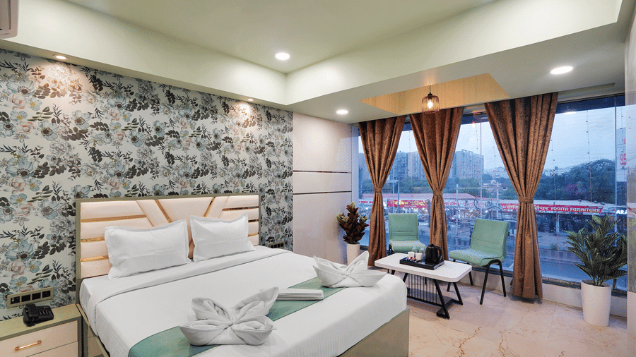 A king size bed in Deluxe Room with large windows overlooking the city at Hotel Regal Heaven, Pune.