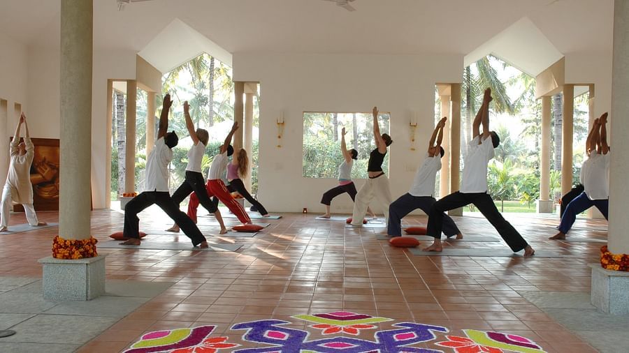 People doing yoga poses in a bright room, colorful rangoli on floor - Shreyas Retreat