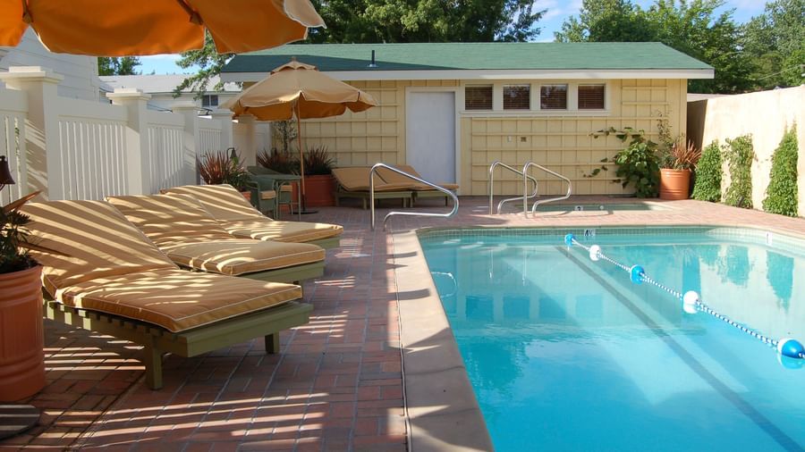 A view of outdoor pool at Tallman Hotel surrounded by cabins and shaded sun beds with umbrellas.