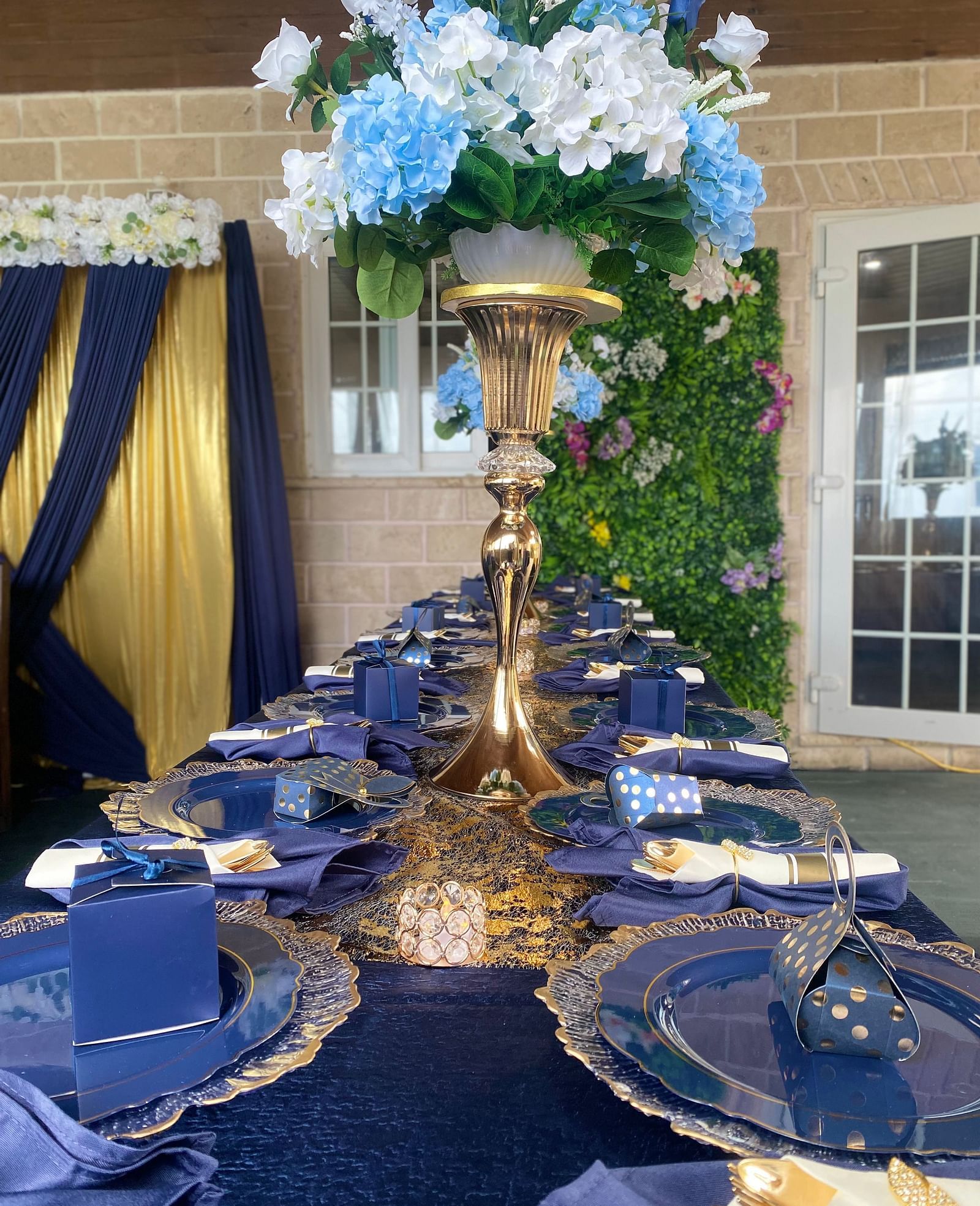 Long banquet table with navy blue napkins, golden cutlery, and tall floral centerpiece | A Stone's Throw Away