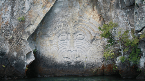 Maori rock carving of a face on a cliff overlooking a lake.