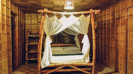 Standard Bamboo Suite at Flower Island Resort featuring a wooden canopy double bed,  bright lighting, and bamboo flooring.